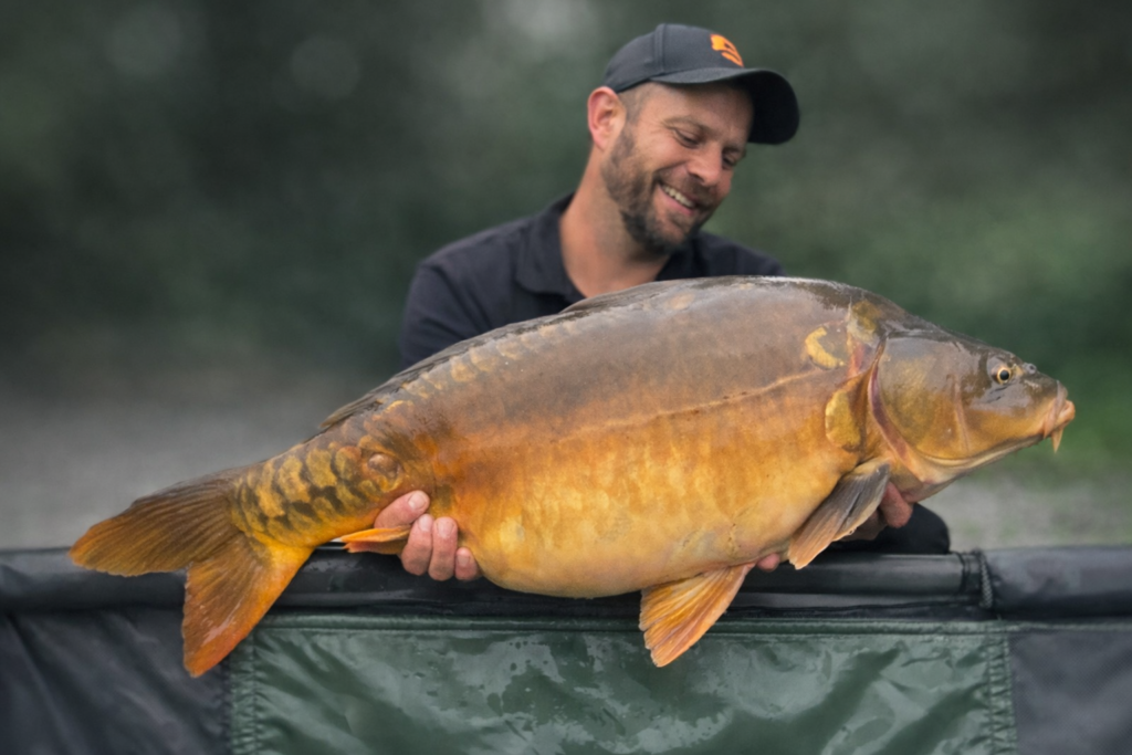 homme souriant avec une carpe miroir
